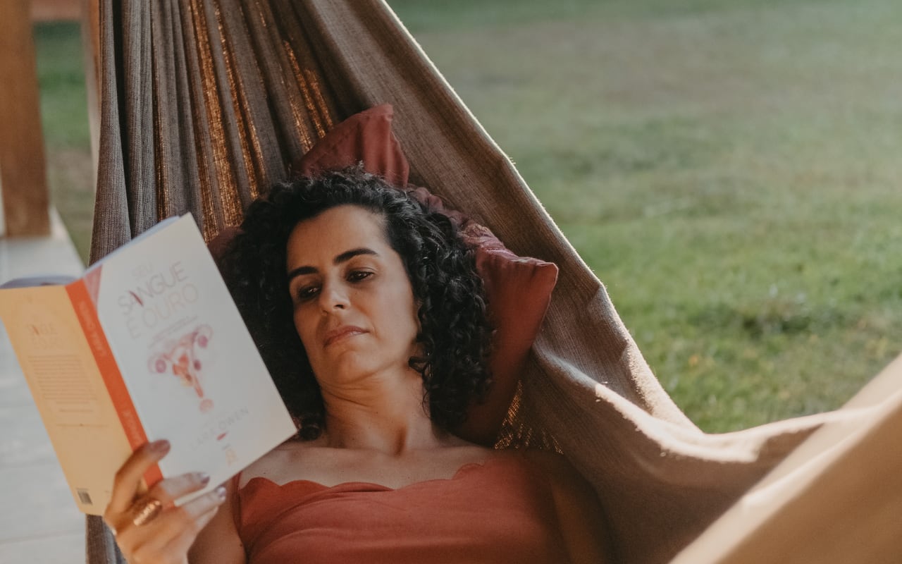 Lu Cerqueira descansando numa rede, lendo sobre os ciclos femininos