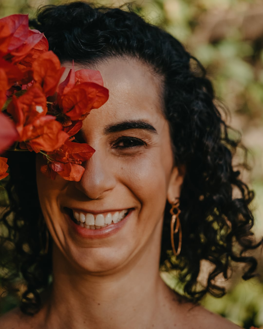 Lu Cerqueira sorrindo, com flores vermelhas junto ao rosto